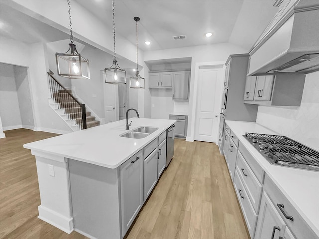 kitchen featuring gray cabinets, custom range hood, a sink, light wood-style floors, and appliances with stainless steel finishes