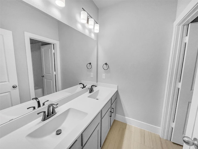 full bathroom featuring double vanity, wood finished floors, baseboards, and a sink