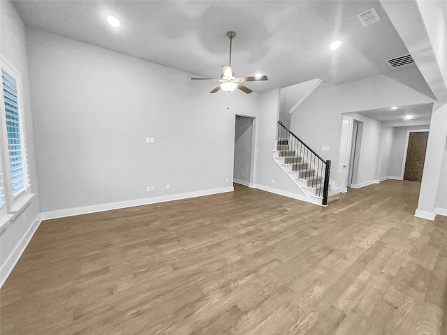 unfurnished living room with visible vents, a ceiling fan, wood finished floors, baseboards, and stairs