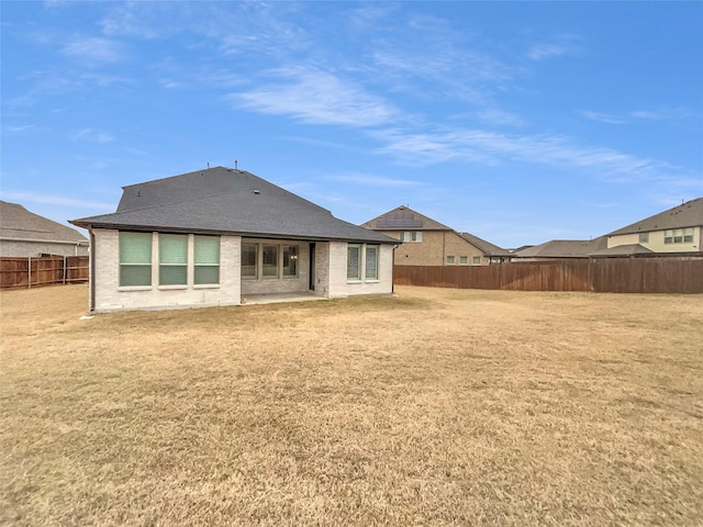 rear view of house with brick siding, a fenced backyard, a lawn, and a shingled roof