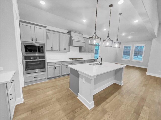 kitchen with a sink, gray cabinetry, stainless steel appliances, custom range hood, and light wood-style floors