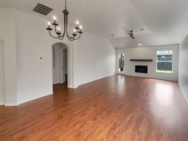 unfurnished living room featuring wood finished floors, visible vents, a fireplace, arched walkways, and ceiling fan with notable chandelier