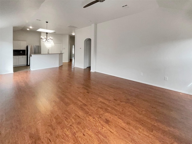 unfurnished living room with ceiling fan with notable chandelier, wood finished floors, arched walkways, baseboards, and vaulted ceiling