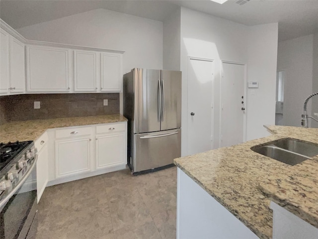 kitchen with a sink, backsplash, white cabinetry, stainless steel appliances, and light stone countertops