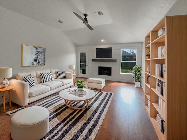 living area with a ceiling fan, visible vents, a fireplace, vaulted ceiling, and wood-type flooring