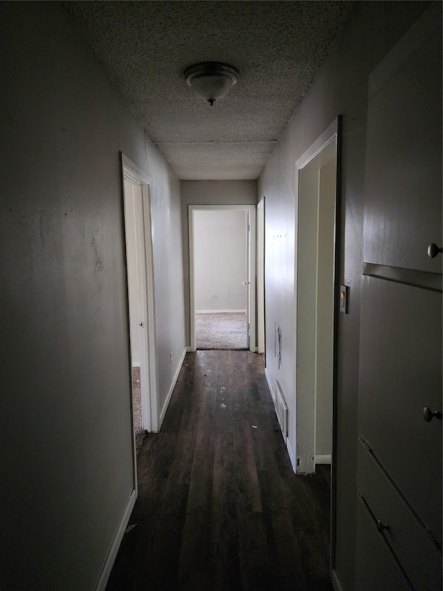 hallway featuring visible vents, baseboards, a textured ceiling, and dark wood-style floors