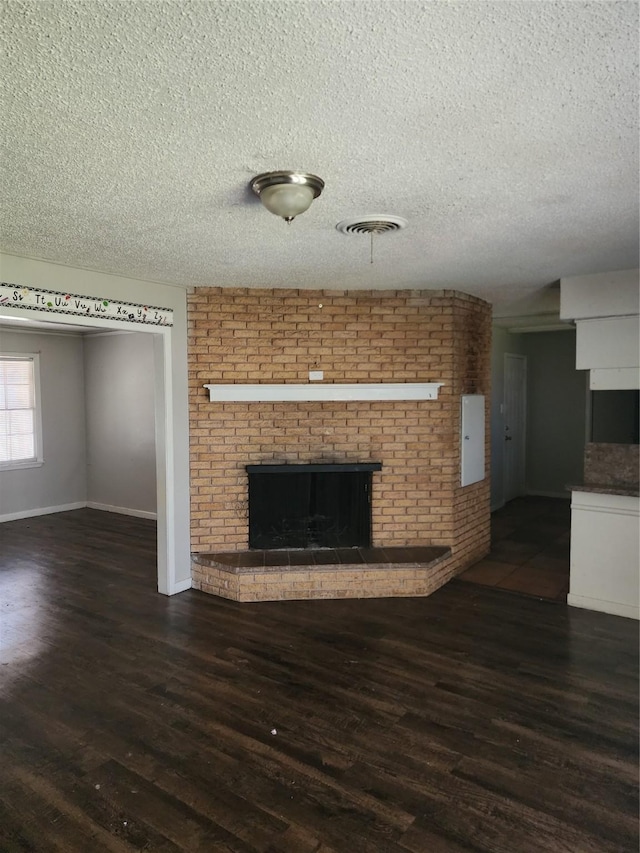 unfurnished living room featuring a brick fireplace, wood finished floors, and a textured ceiling