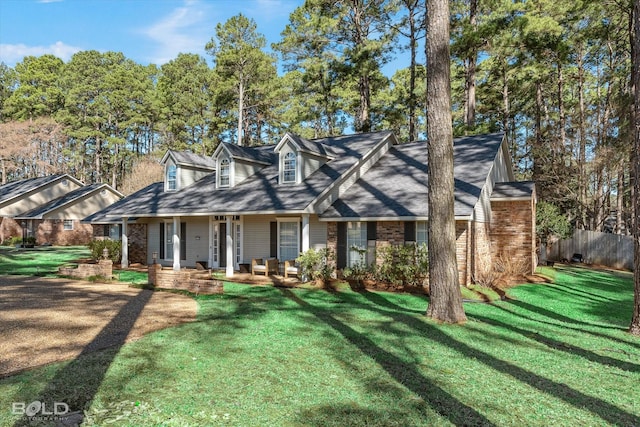 new england style home with brick siding, covered porch, a front lawn, and fence