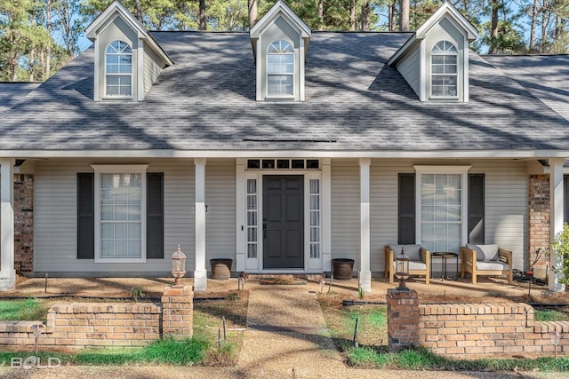 cape cod house with brick siding, covered porch, and roof with shingles