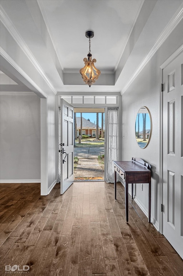 entryway with a notable chandelier, a raised ceiling, dark wood-type flooring, and crown molding