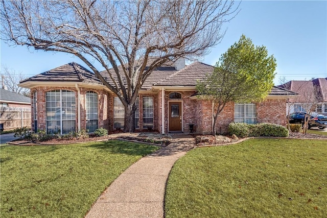 ranch-style home with brick siding, a chimney, a front lawn, and fence