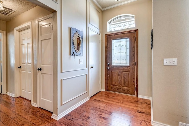 foyer entrance with light wood-type flooring, visible vents, baseboards, and ornamental molding