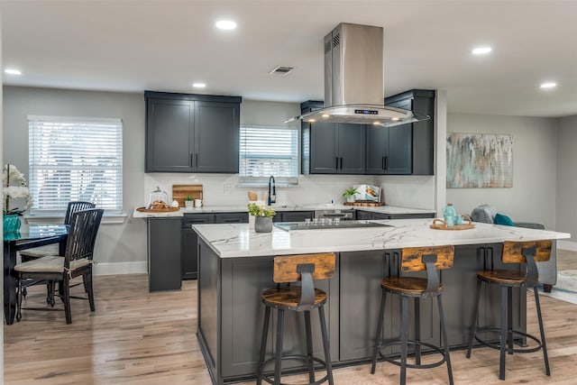 kitchen featuring tasteful backsplash, a breakfast bar area, light stone counters, and island range hood