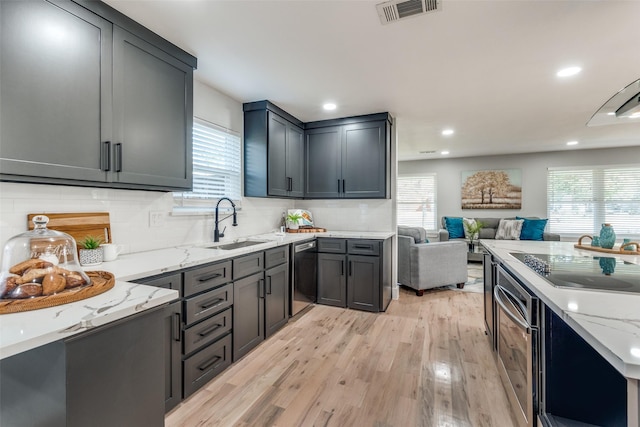 kitchen featuring visible vents, light wood-type flooring, light stone counters, open floor plan, and dishwashing machine