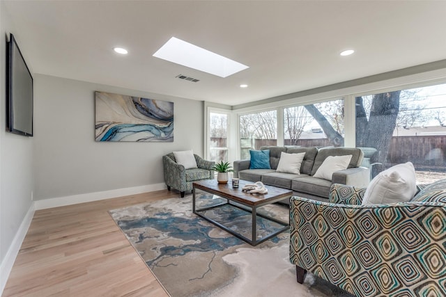 living area with a skylight, recessed lighting, wood finished floors, and baseboards