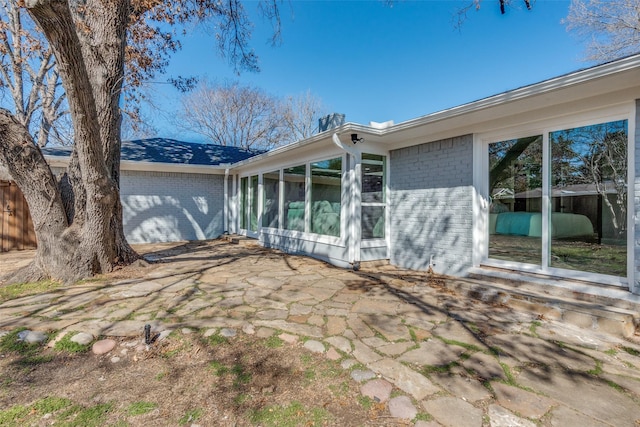 back of property featuring brick siding, a patio area, fence, and a sunroom