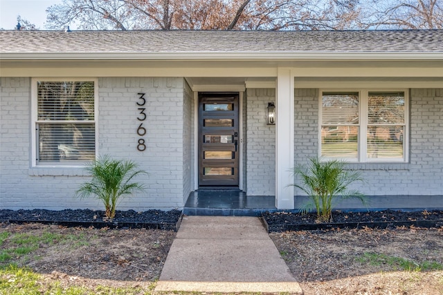 view of exterior entry featuring brick siding, a porch, and a shingled roof