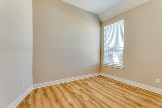 empty room with lofted ceiling, light wood-type flooring, and baseboards