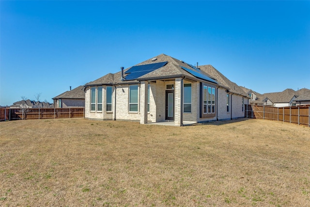 rear view of property featuring a yard, roof mounted solar panels, brick siding, and a fenced backyard