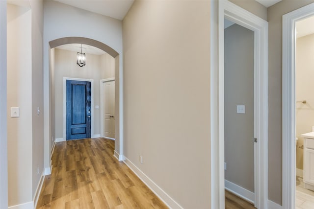 hallway featuring arched walkways, light wood finished floors, and baseboards