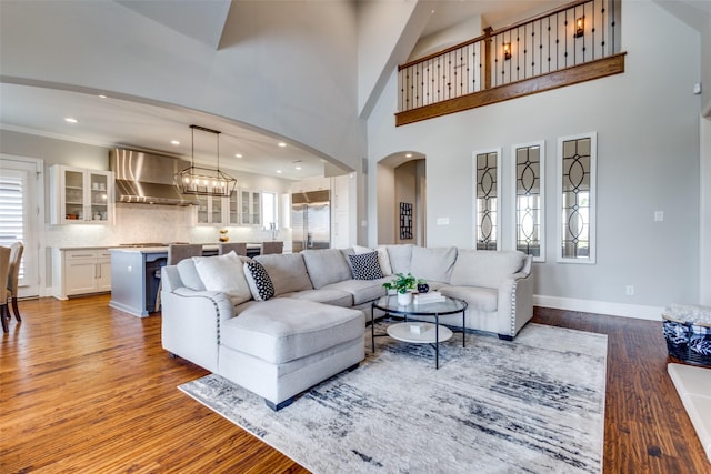 living area featuring wood finished floors, arched walkways, a high ceiling, baseboards, and a chandelier