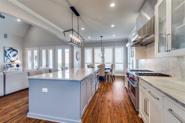 kitchen featuring range with two ovens, light stone countertops, wall chimney exhaust hood, and white cabinetry