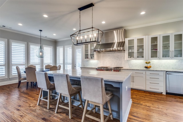 kitchen with visible vents, a kitchen island, stainless steel dishwasher, crown molding, and wall chimney range hood