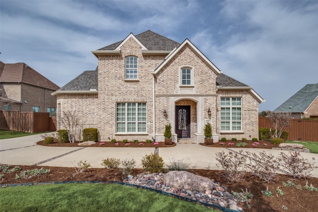 french country style house featuring brick siding, a shingled roof, and fence