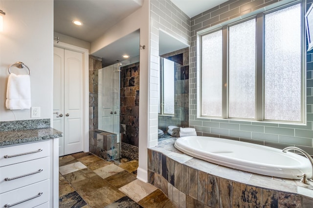 full bath with vanity, recessed lighting, stone finish floor, walk in shower, and a garden tub