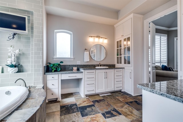 full bath featuring vanity, a garden tub, stone finish floor, and ornamental molding