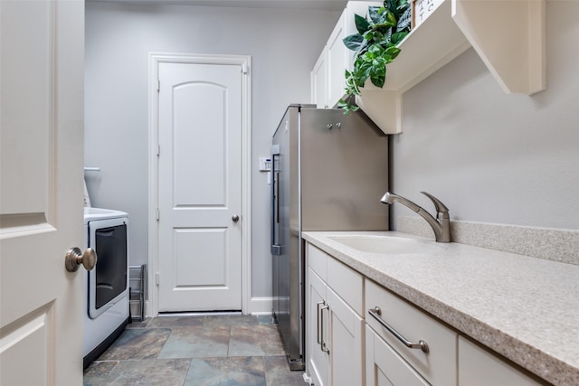 washroom featuring stone finish floor, washer / clothes dryer, cabinet space, and a sink