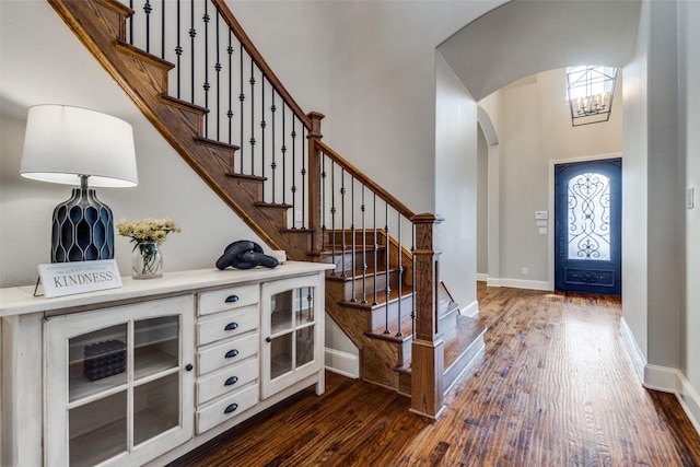 foyer entrance with plenty of natural light, arched walkways, dark wood-style flooring, and baseboards