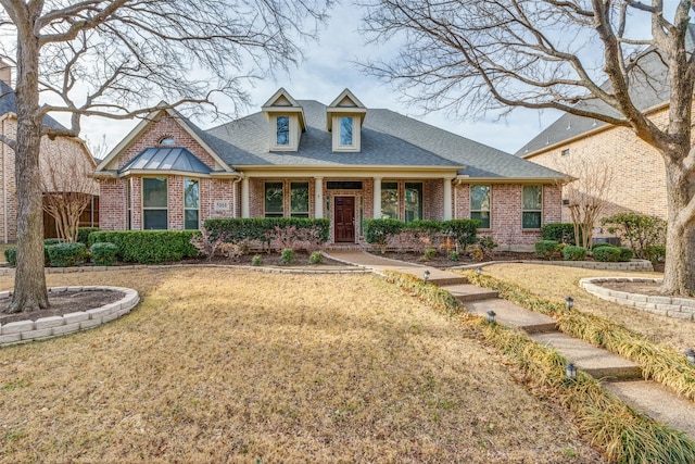 view of front of house featuring brick siding, a front lawn, and a shingled roof