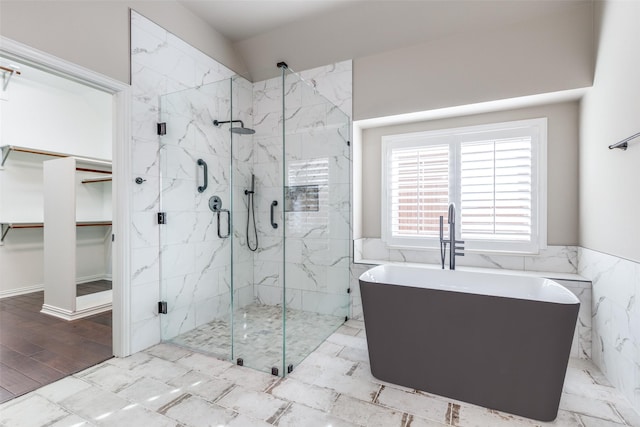 full bath with a walk in closet, a soaking tub, a wainscoted wall, and a marble finish shower