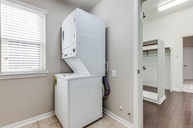 laundry room featuring stacked washer / drying machine, baseboards, wood finished floors, and laundry area