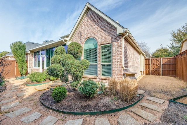 view of side of home featuring brick siding, a gate, and fence