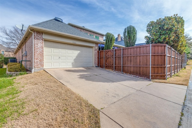 view of home's exterior featuring fence, roof with shingles, concrete driveway, central air condition unit, and brick siding