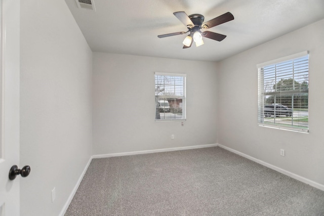 carpeted spare room with visible vents, a ceiling fan, and baseboards