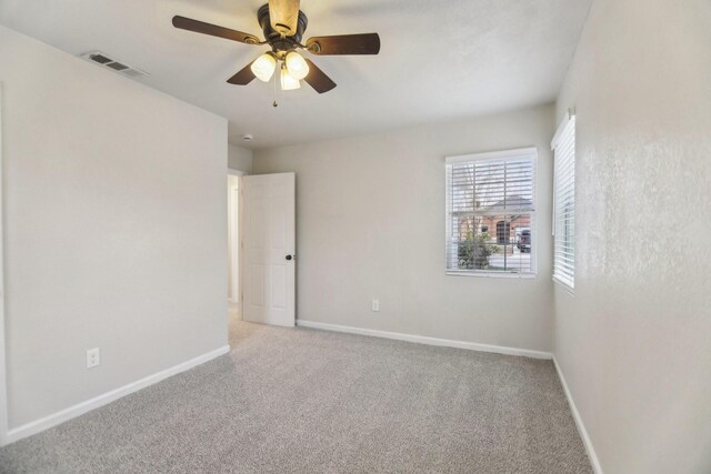 empty room with visible vents, light colored carpet, a ceiling fan, and baseboards