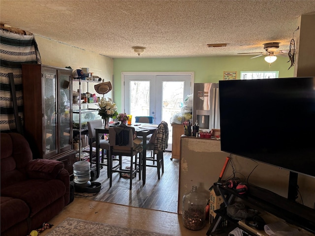 dining room with french doors, a textured ceiling, ceiling fan, and wood finished floors