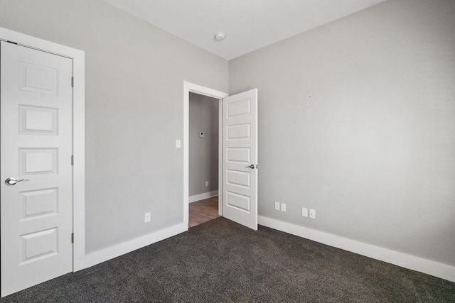 unfurnished room with dark colored carpet and baseboards