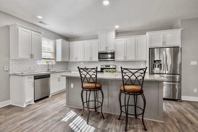 kitchen with visible vents, wood finished floors, a center island, stainless steel appliances, and white cabinets