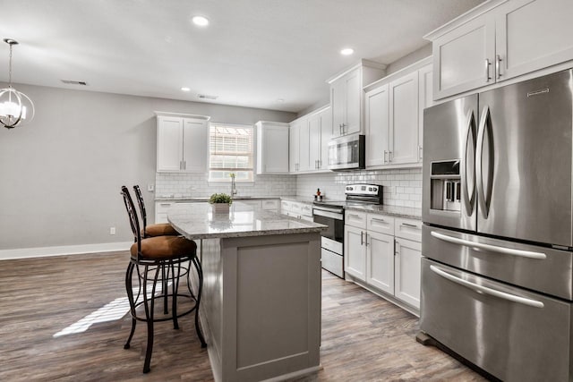 kitchen with backsplash, a kitchen island, white cabinetry, stainless steel appliances, and a breakfast bar area