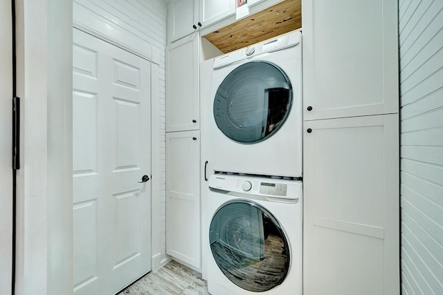 laundry area featuring light wood finished floors, cabinet space, and stacked washing maching and dryer