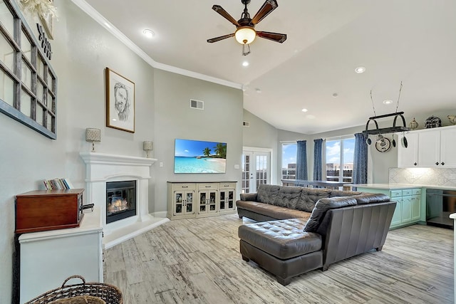 living area featuring visible vents, ceiling fan, light wood-type flooring, ornamental molding, and a glass covered fireplace