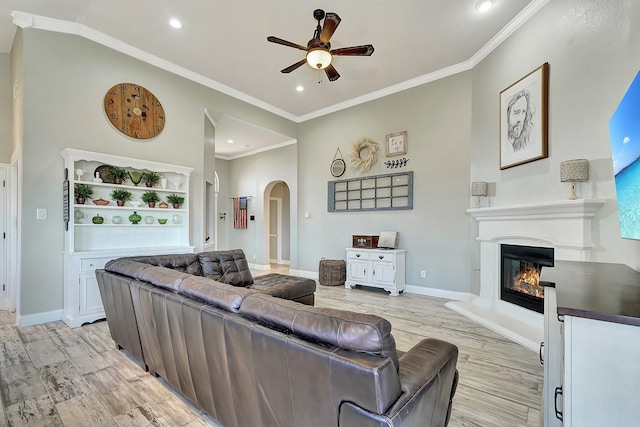 living room featuring light wood-type flooring, a glass covered fireplace, arched walkways, baseboards, and ceiling fan