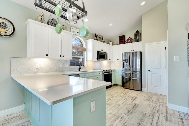 kitchen with a peninsula, a sink, stainless steel appliances, light countertops, and backsplash