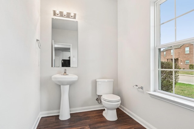 half bathroom with toilet, wood finished floors, and baseboards