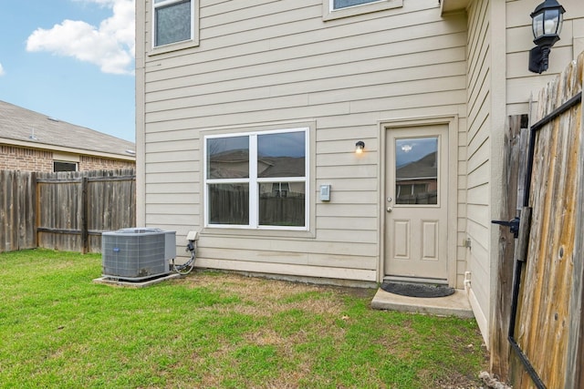 property entrance with central air condition unit, a lawn, and fence