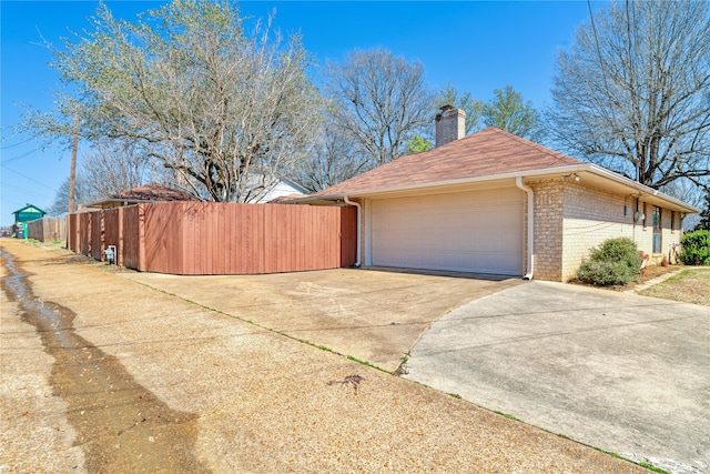 view of side of property featuring fence, an attached garage, a chimney, concrete driveway, and brick siding